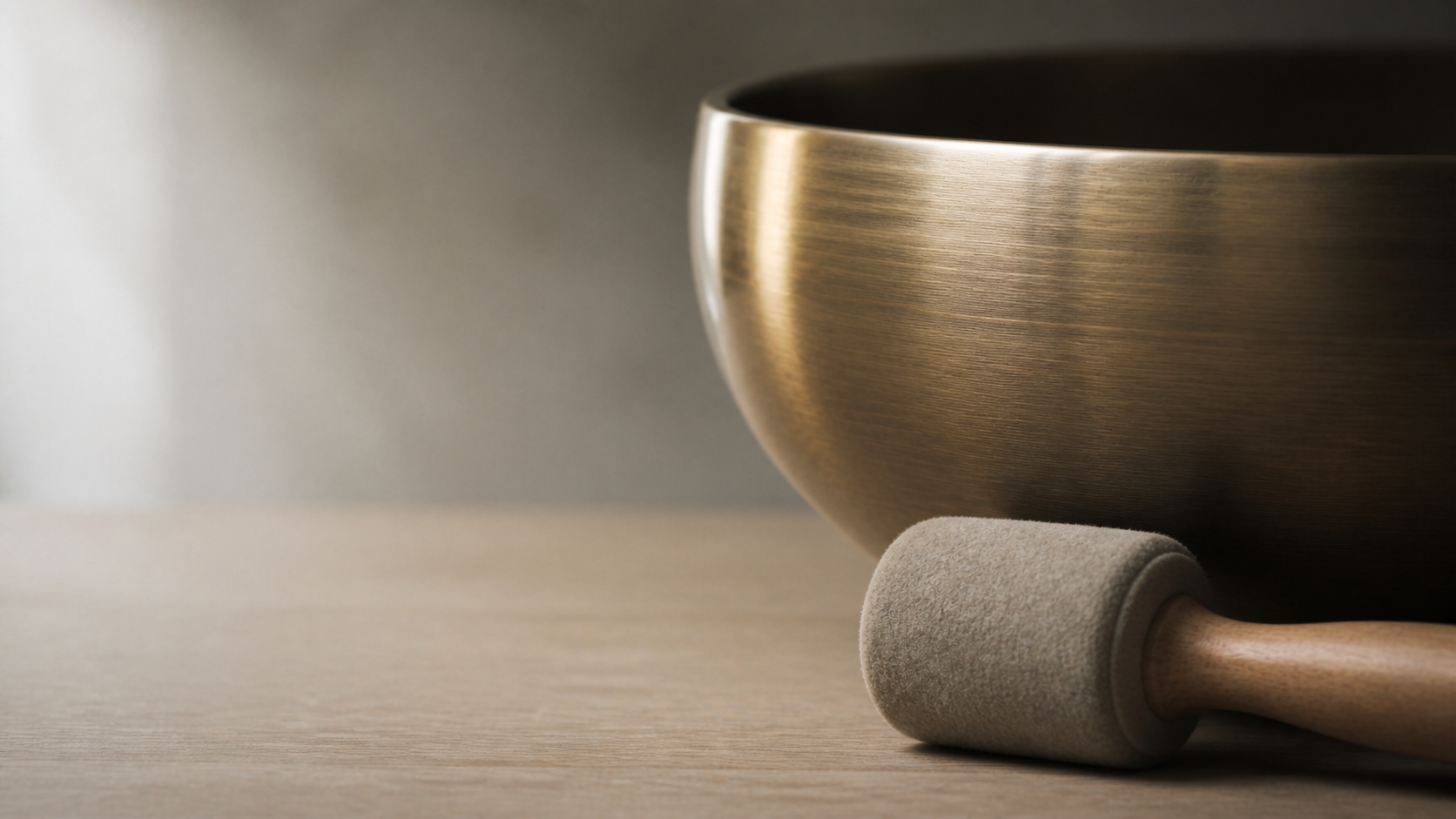 Brushed bronze singing bowl and felt mallet on pale oak with clean negative space