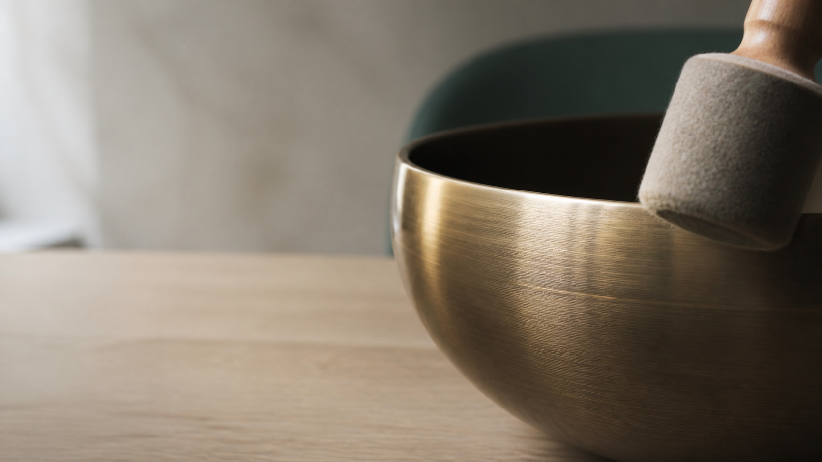 Extreme macro of a felt mallet touching the rim of a brushed bronze singing bowl
