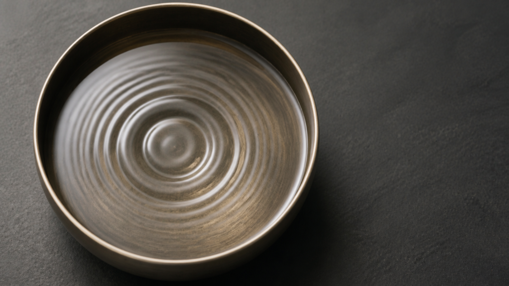 Overhead macro of concentric water ripples in a shallow bowl on dark slate